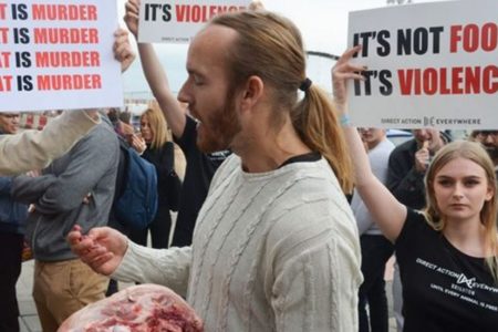 Hombre come cabeza de cerdo cruda frente a festival de vegetarianos